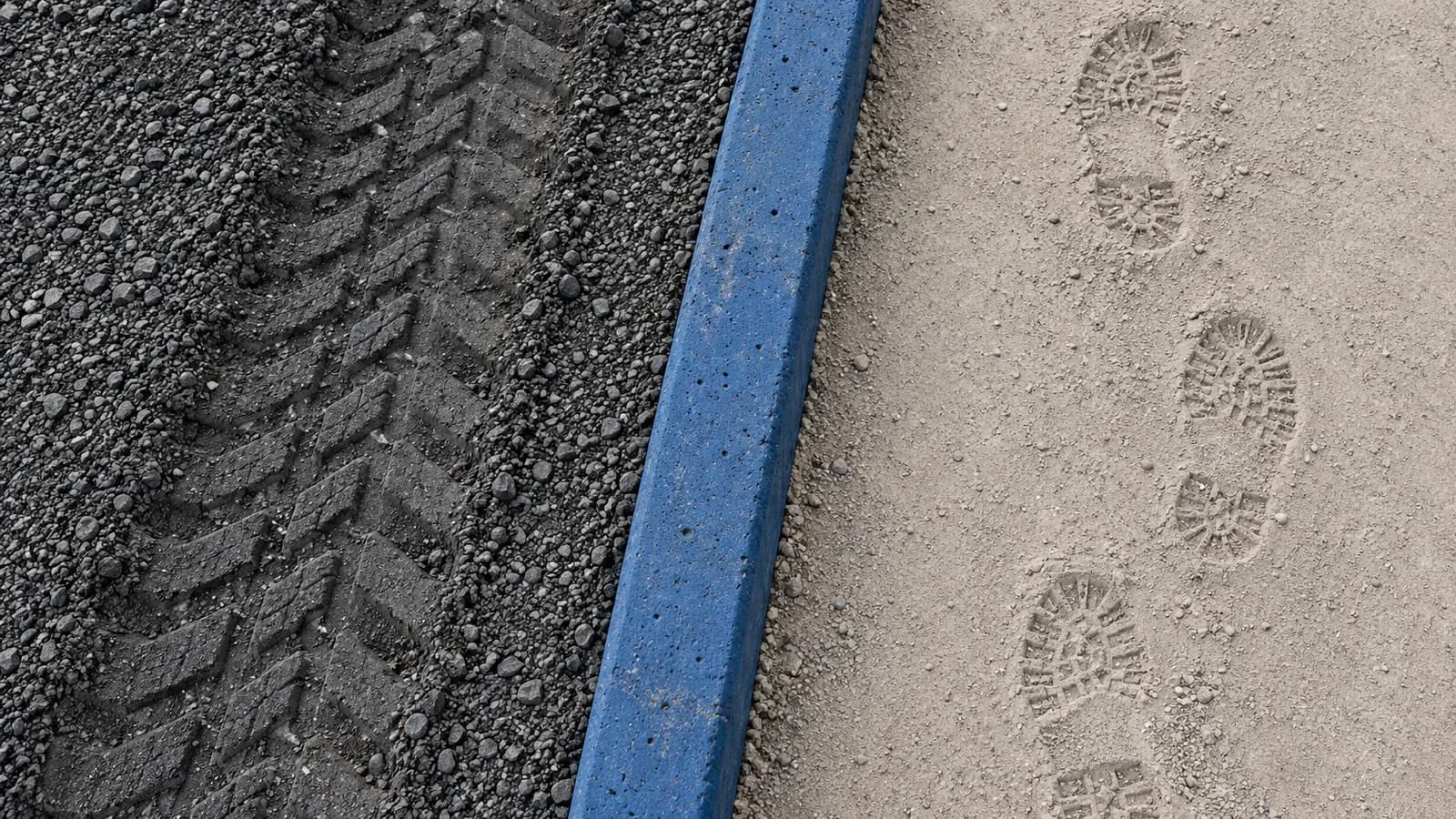 Farklı mineral yüzeylerde lastik ve iş ayakkabısı izlerini ayıran kobalt mavisi beton ayırıcının üstten görünüşü; editoryal bir metafor.