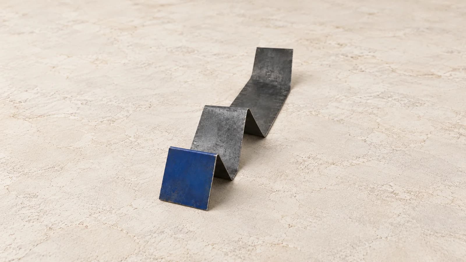 A short cobalt face begins a longer folded charcoal metal strip.